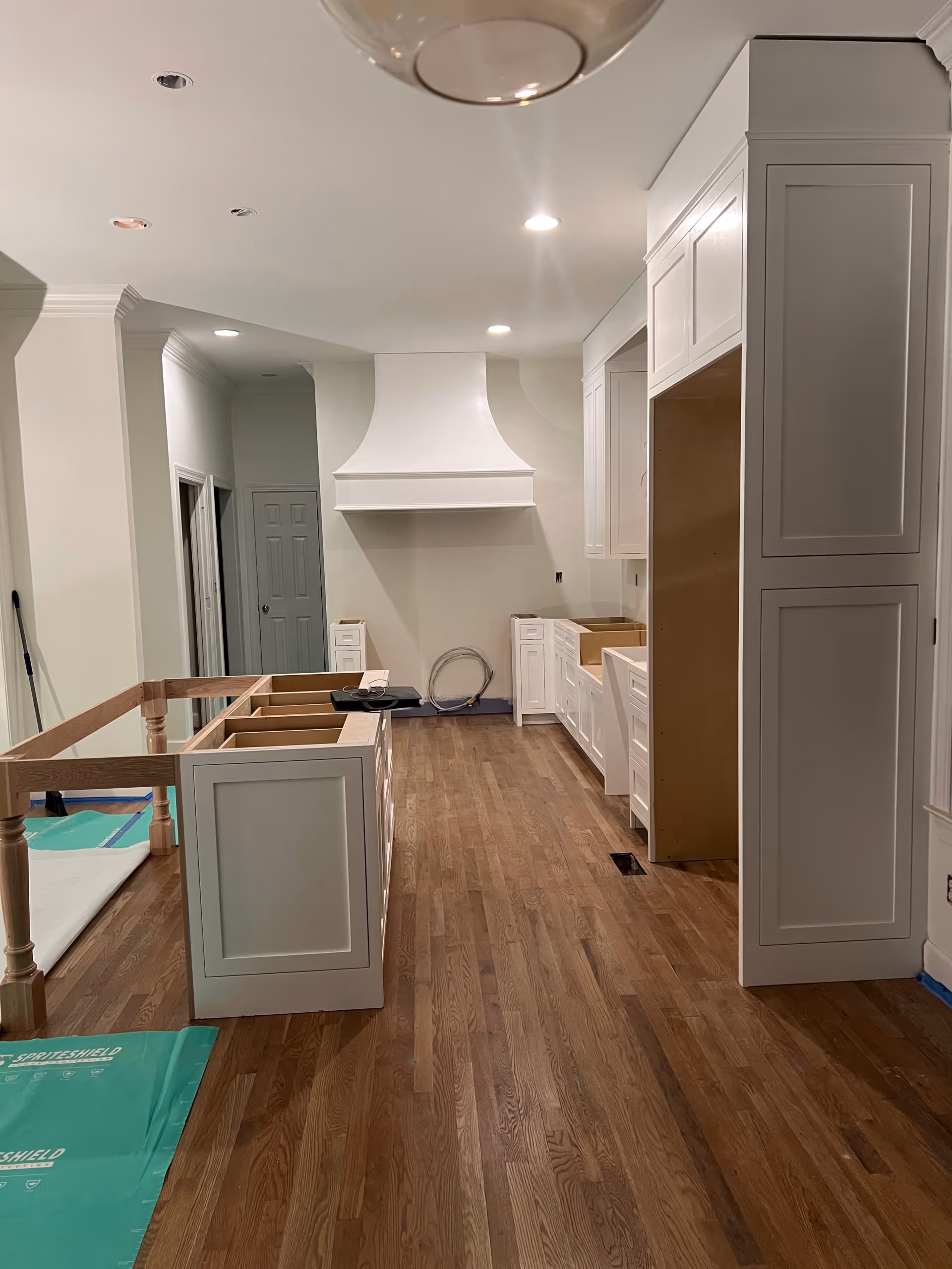 White cabinetry and a range hood are installed in a spacious, under-construction kitchen.