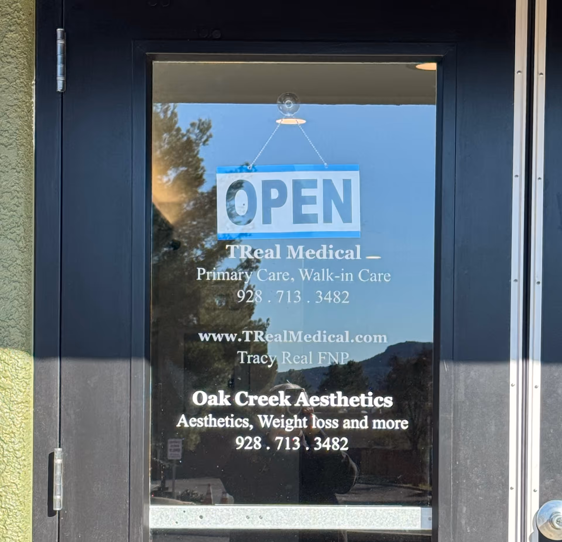 Front entrance glass door displaying OPEN sign and TReal Medical contact information.