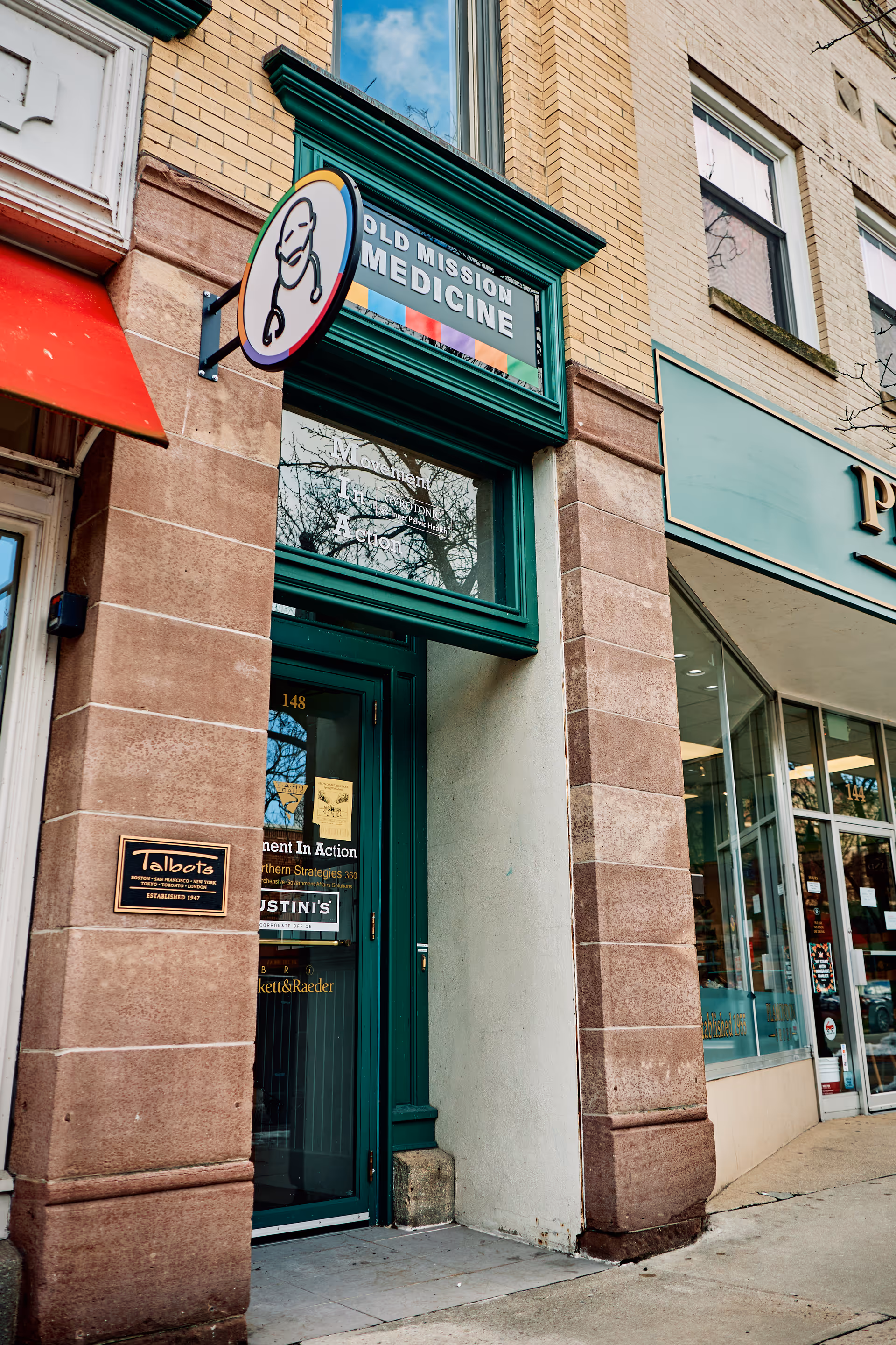 Exterior storefront with Old Mission Medicine sign and green doorway on brick building.