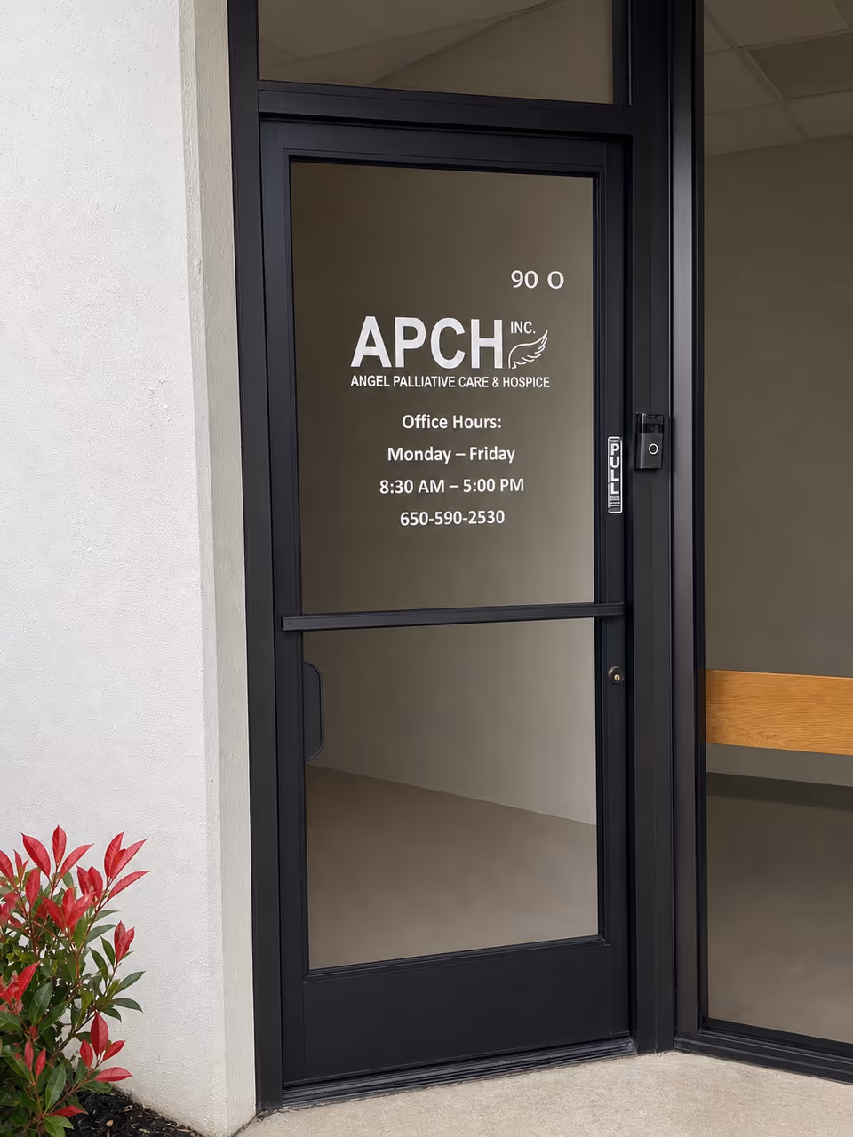 Glass door entrance to Angel Palliative Care & Hospice with exterior wall and plants.