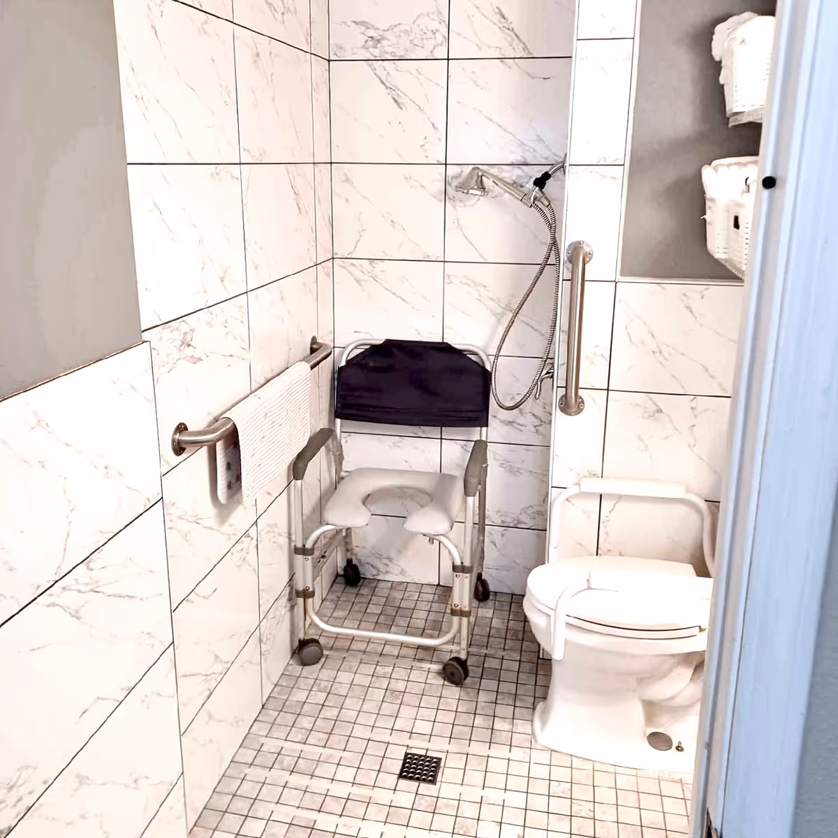 Accessible bathroom with a shower chair, grab bars, and a toilet in tiled space.