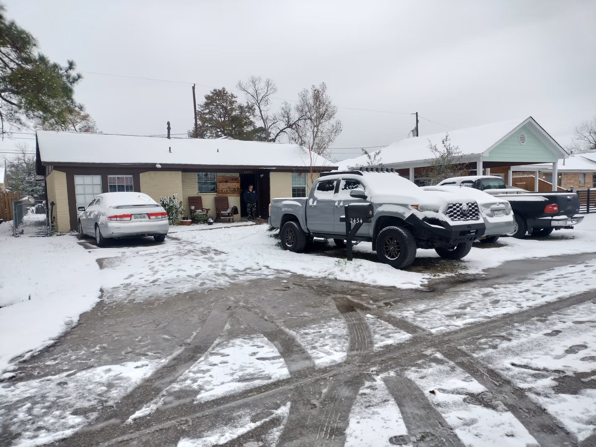 Snow-covered single-story care home exterior with parked vehicles and a person near the entrance.