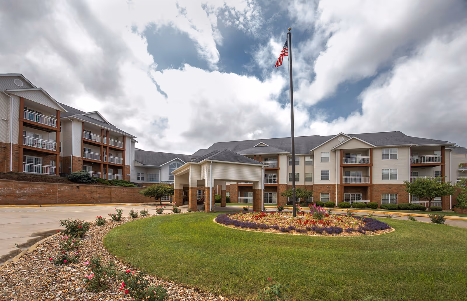 Exterior view of a senior living facility with a circular flower bed and flagpole.