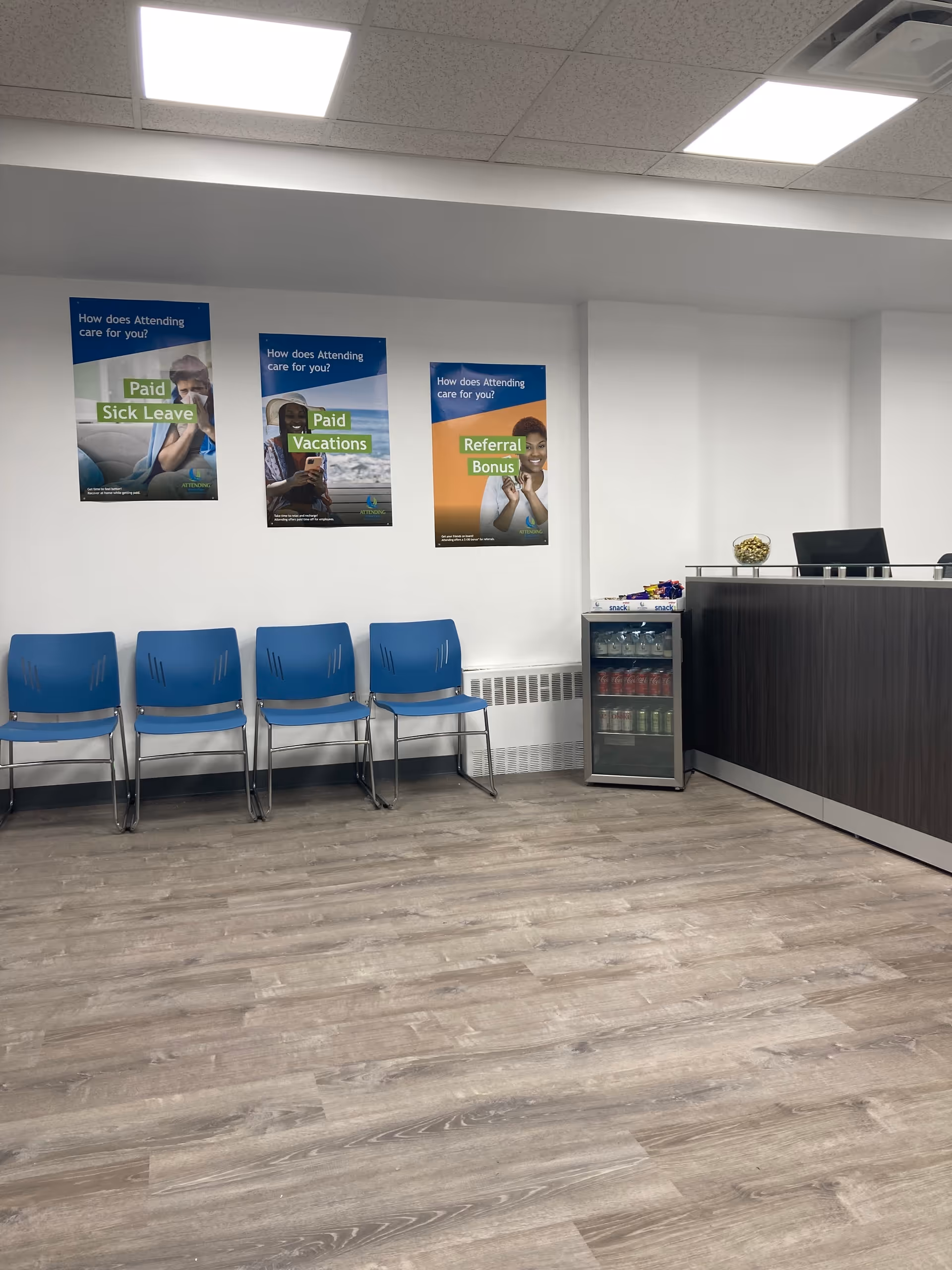 Waiting area with blue chairs, posters on the wall, and a dark reception desk.