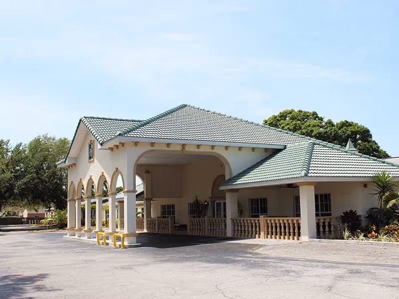 Front entrance of a single-story building with a green tiled roof, arched columns, and a covered porte-cochère.