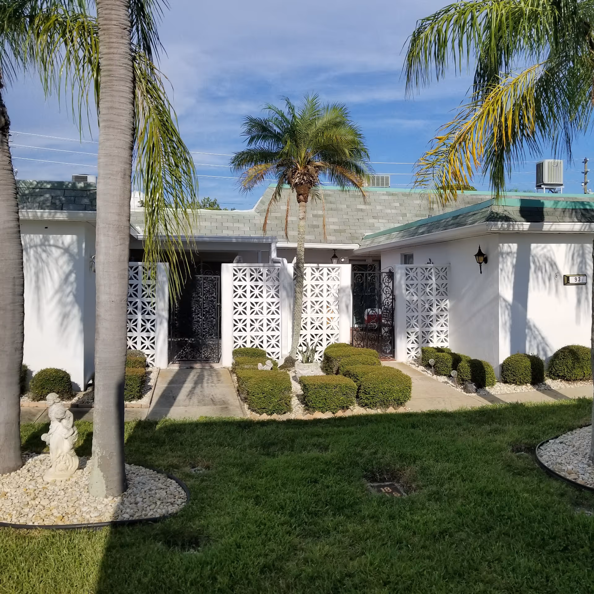 Exterior view of Boca Ciega Point building with palm trees, gated entry, and manicured shrubs.