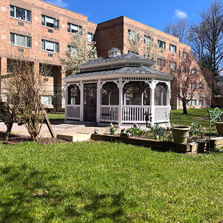 White gazebo in a courtyard with a brick building and green lawn.