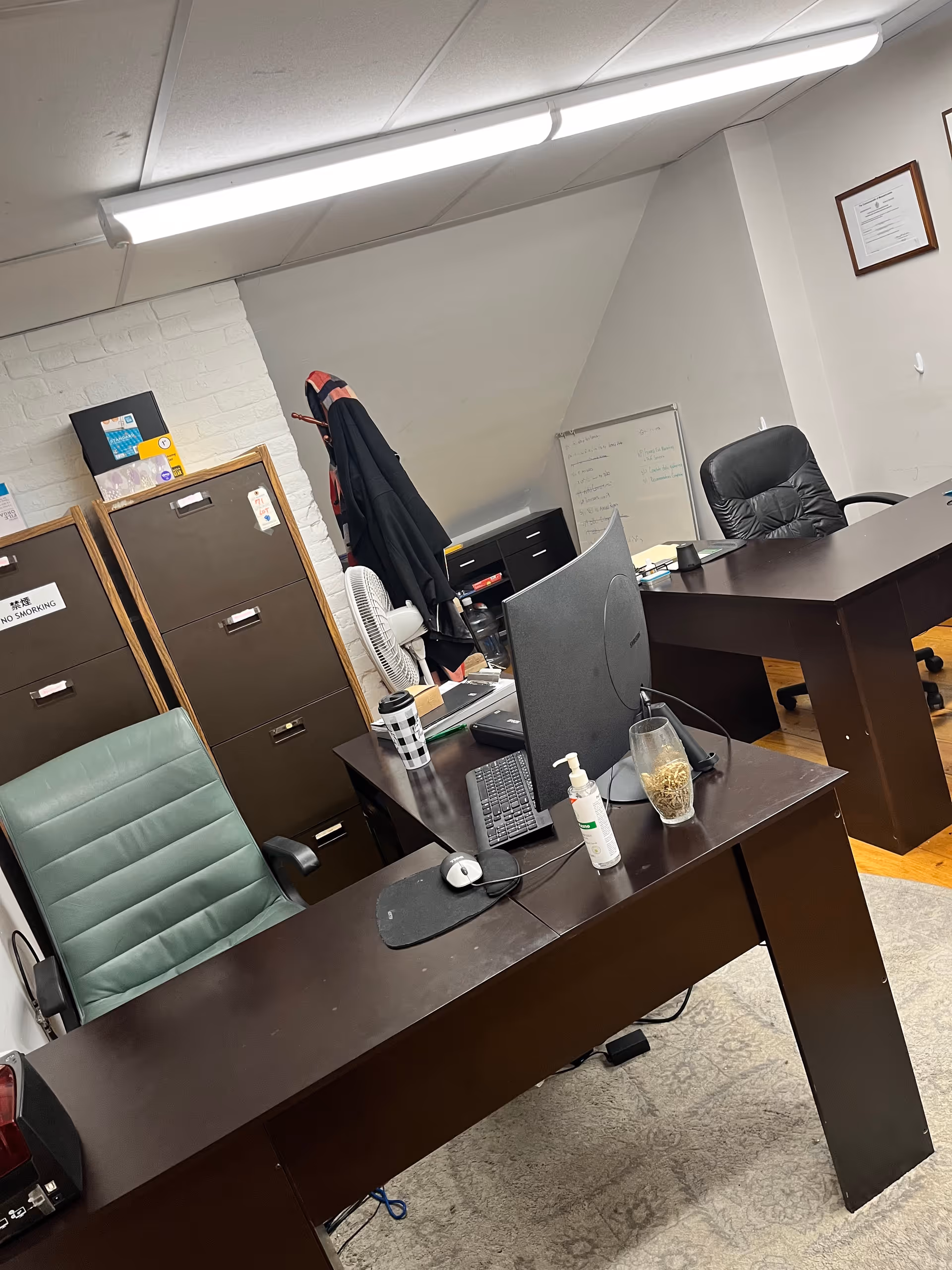 Office workspace with desks, computer monitor, filing cabinets, and a coat hanging.