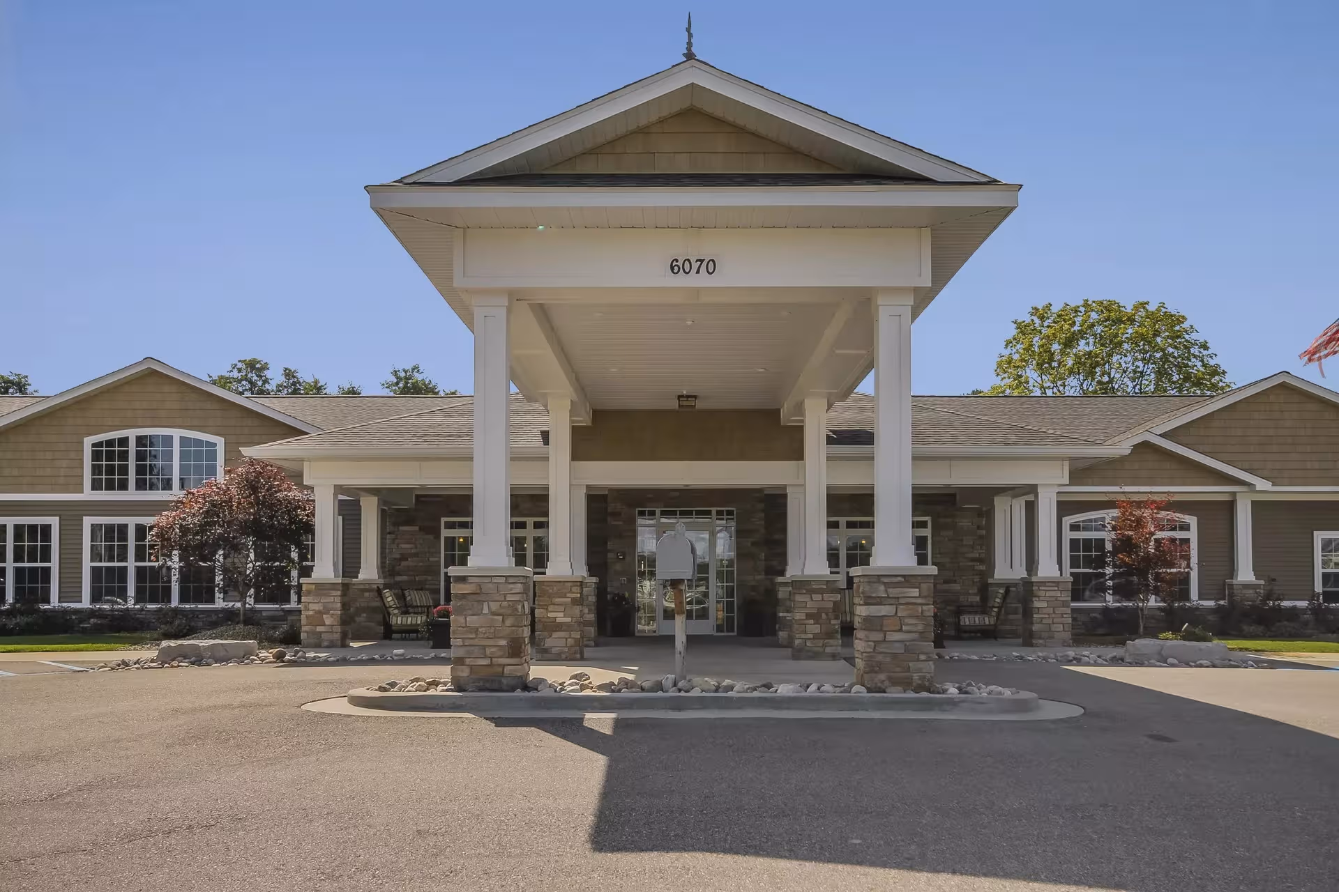 Senior living facility entrance with a covered drop-off, stone columns, and a clear address plaque.