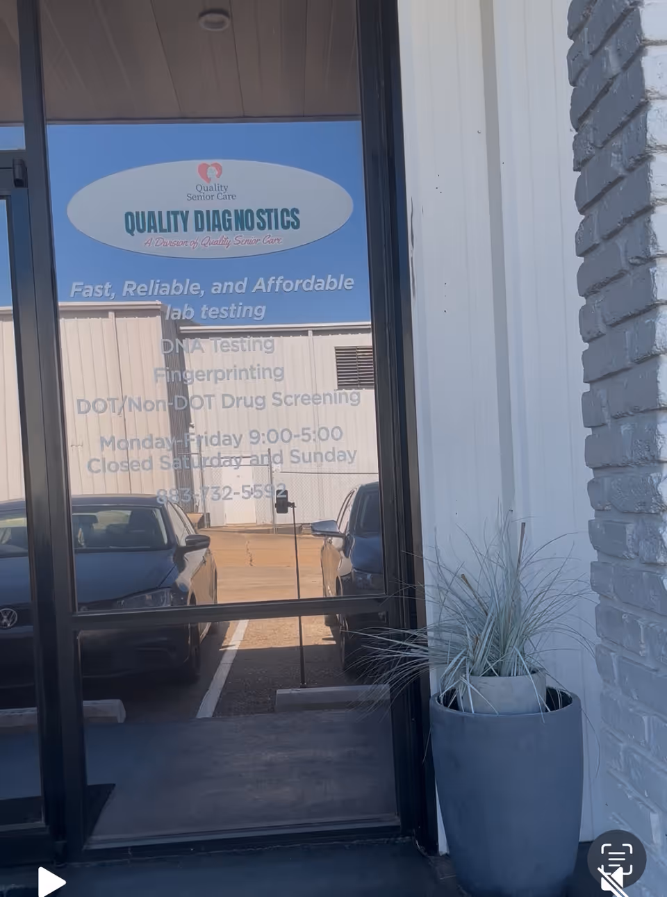 Facility entrance glass door with 'QUALITY DIAGNOSTICS' sign, reflecting parked cars and a potted plant.
