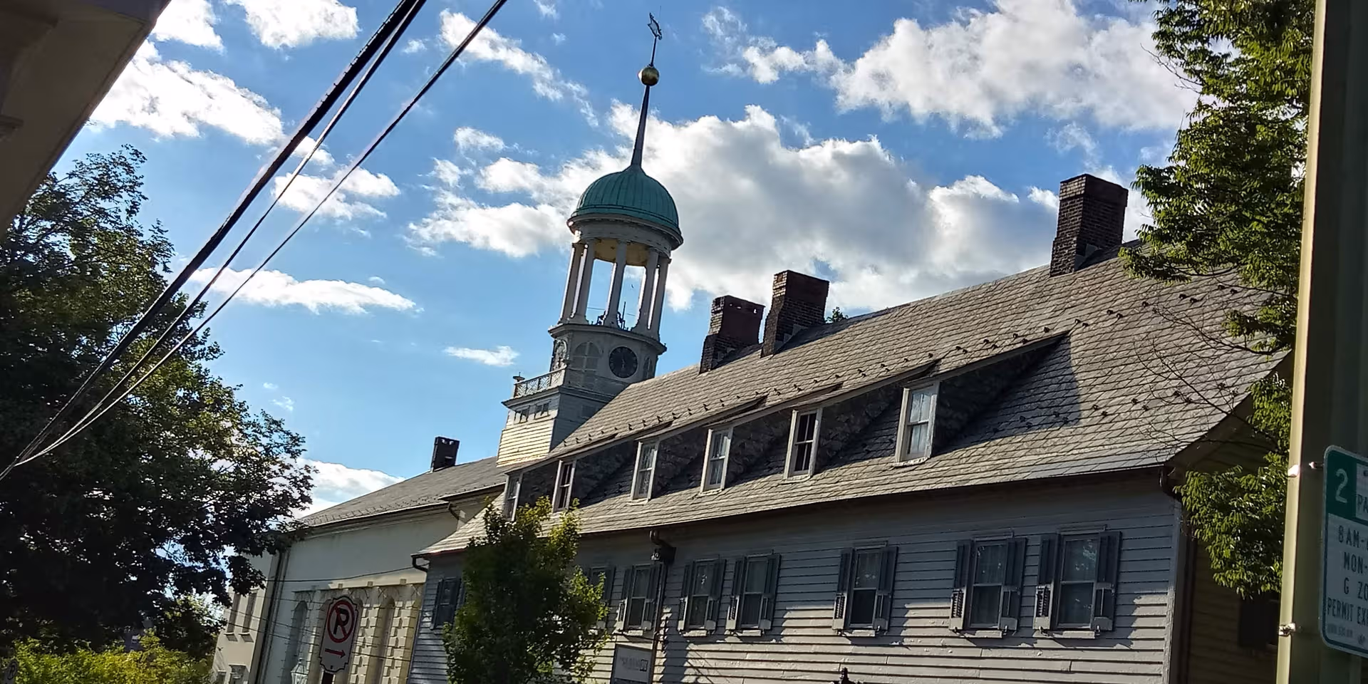Sloped-roofed senior living building with a cupola and shutters against a blue sky.