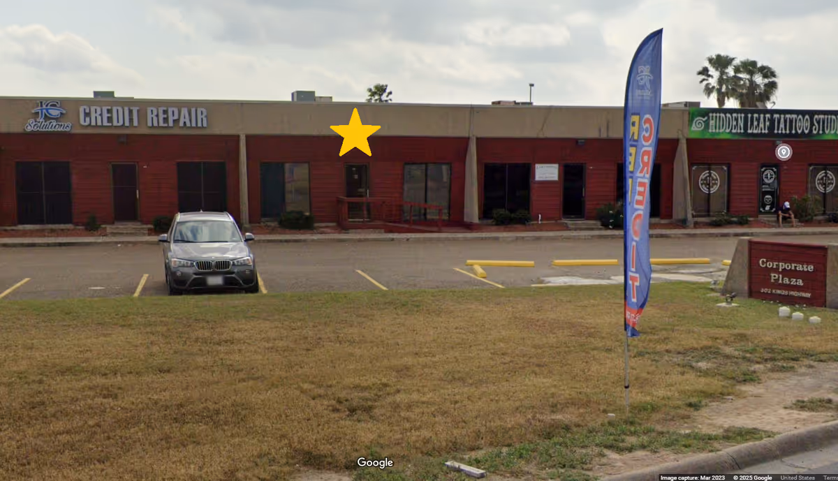 Exterior view of a strip mall with storefronts, a parked car, and a blue sky.