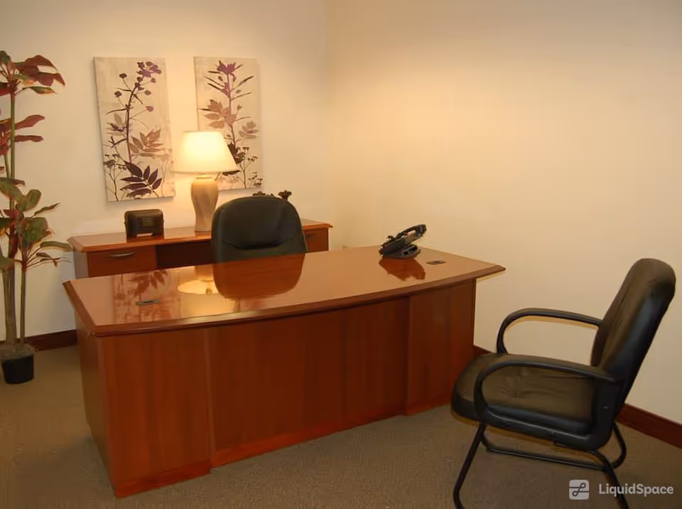 Polished wooden desk with two chairs, lamp, and plant in a small office.