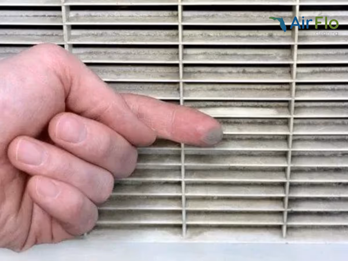Close-up of a hand pointing at a dusty interior air vent grille.