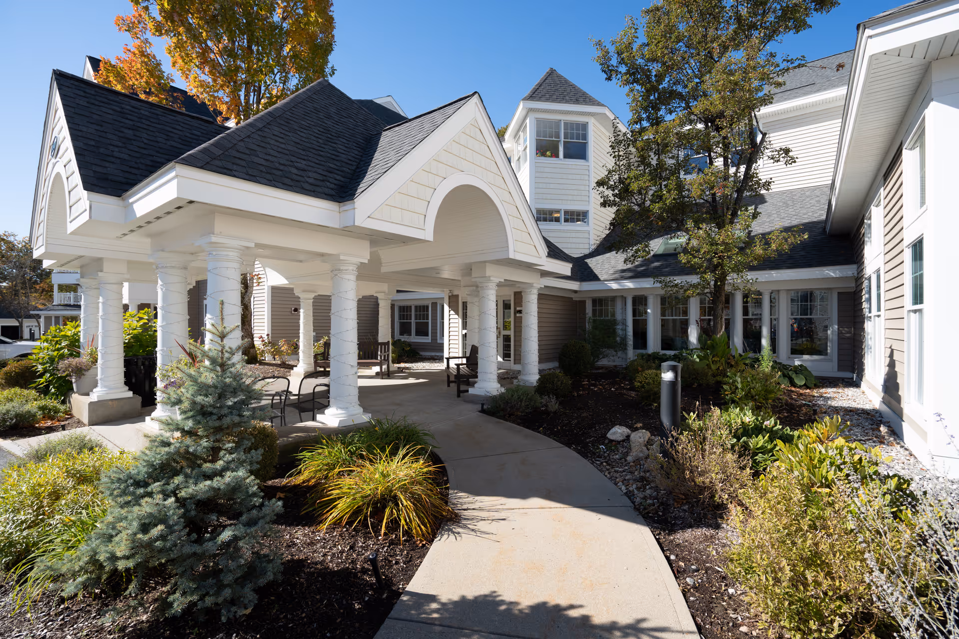 Front exterior of RiverWoods Manchester with a covered entrance, columns, and landscaped pathway.