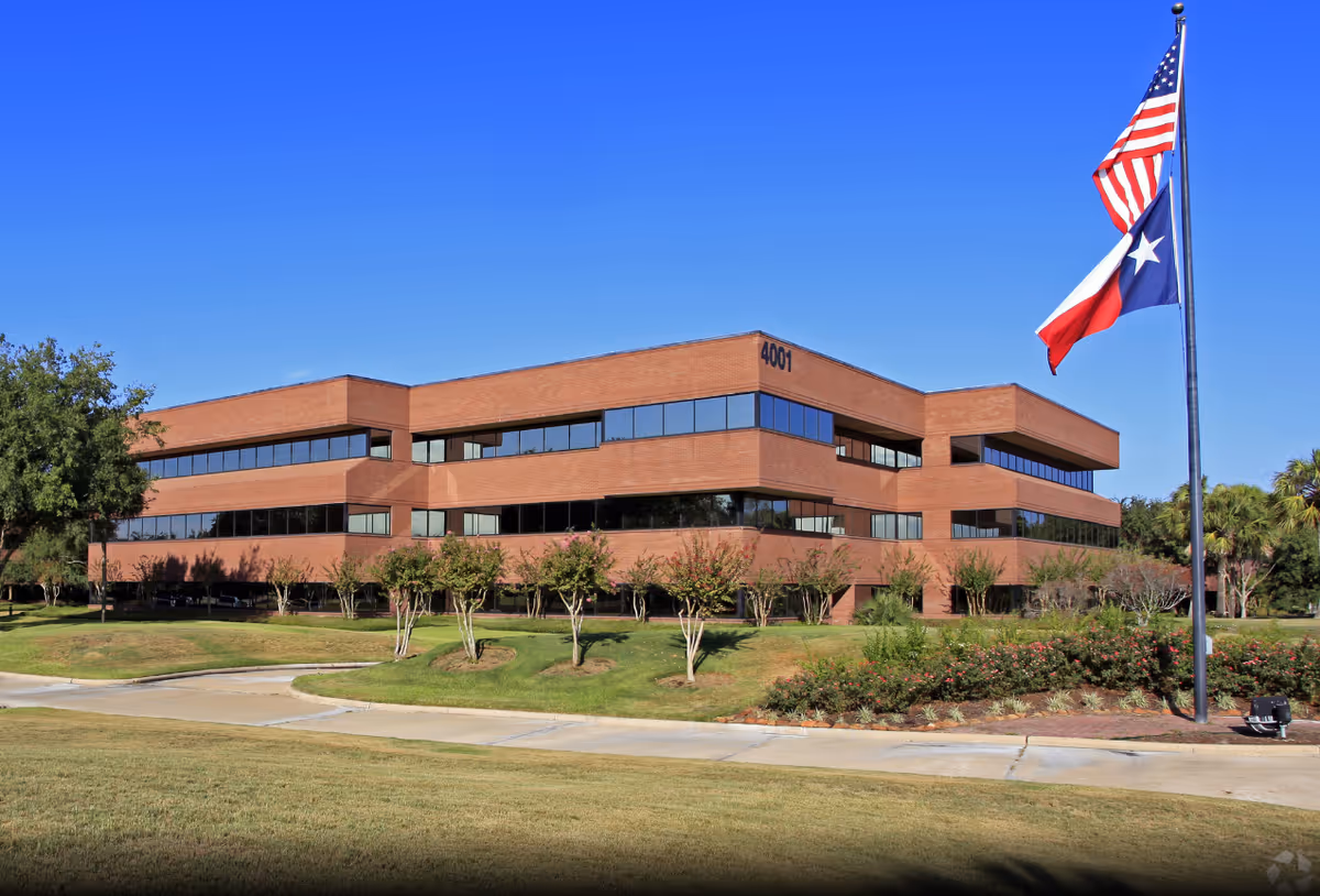 Brick, two-story office building with large windows, a flagpole, and American/Texas flags.