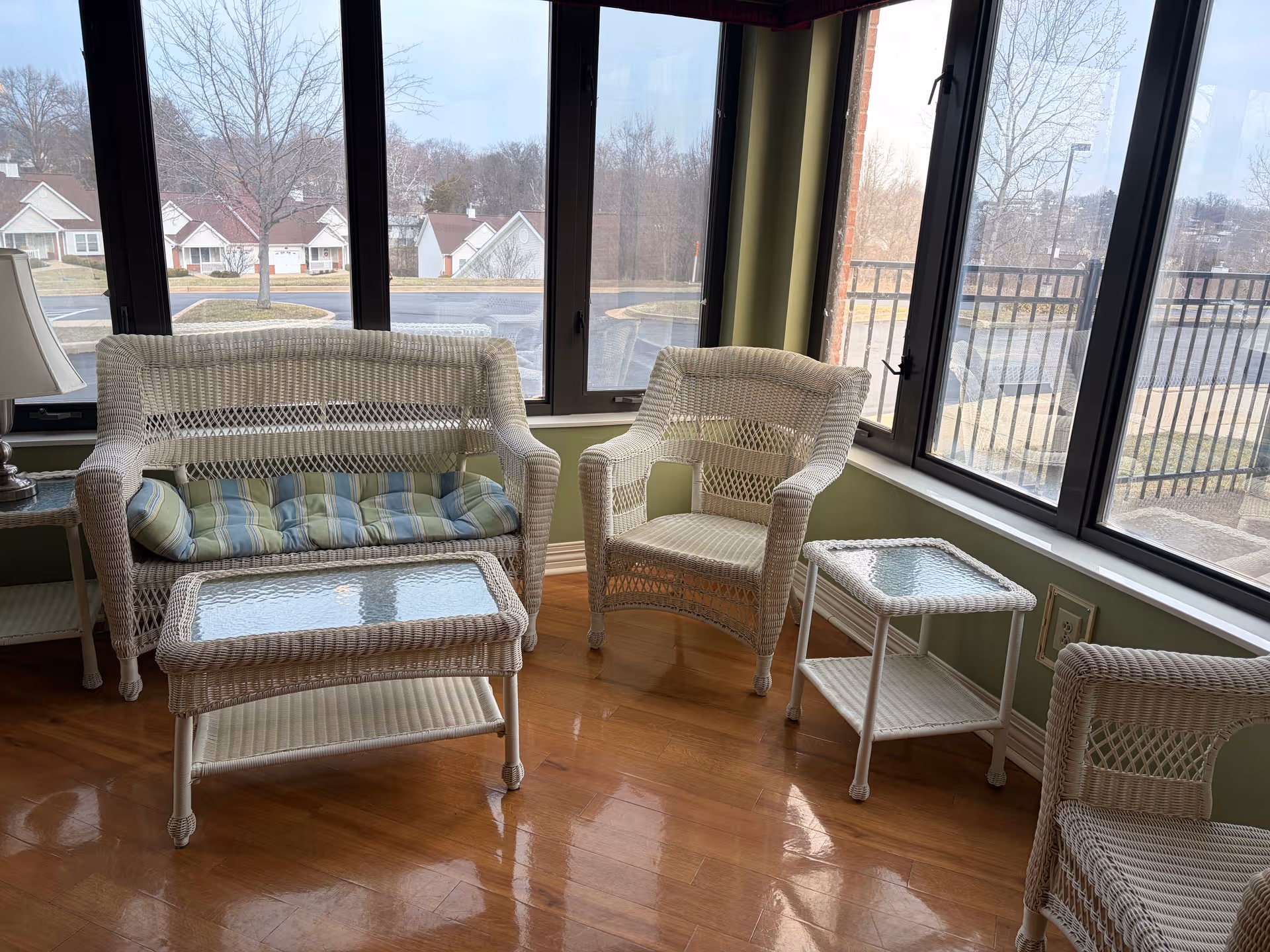 Bright sunroom with white wicker furniture and glass-topped tables by large windows.