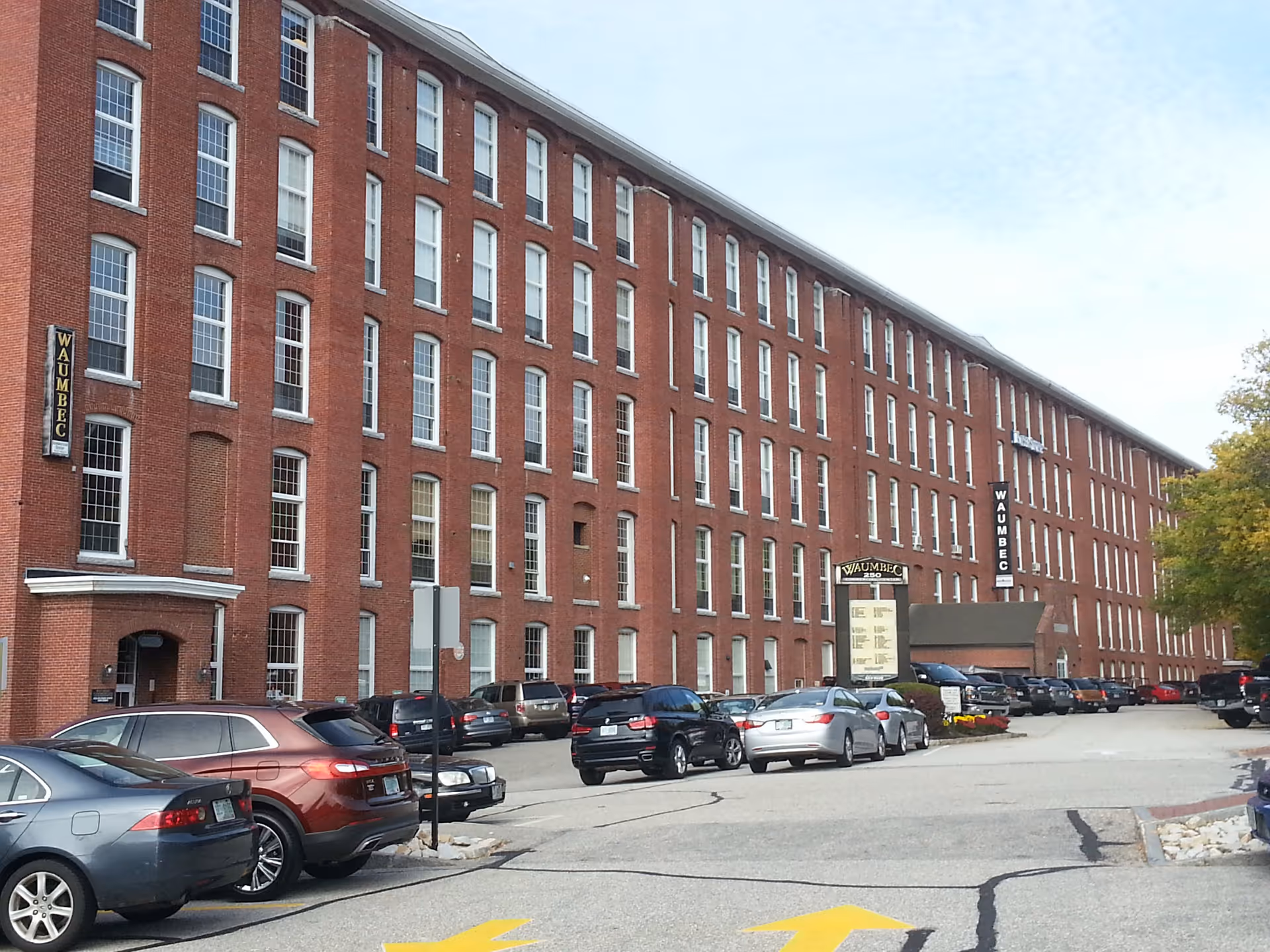 Long red brick building with many windows and parked cars along the street.