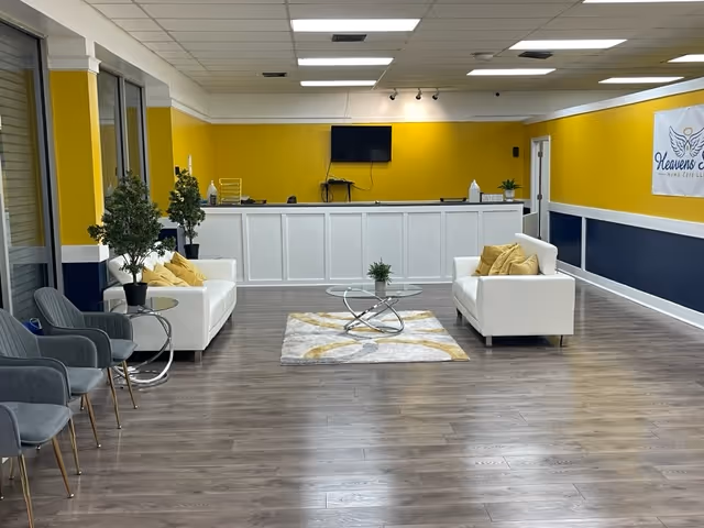Bright yellow lobby with white reception desk, sofas, coffee table, TV, and a Heavens Sent banner.