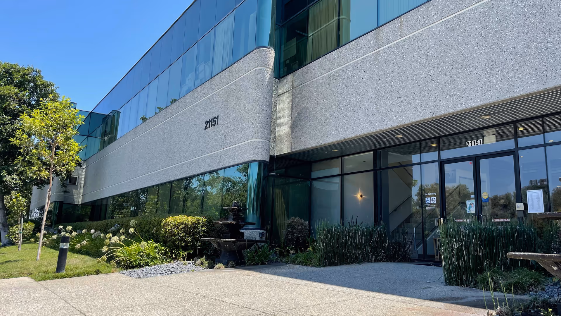 Modern senior living facility exterior with glass façade and landscaped entrance.