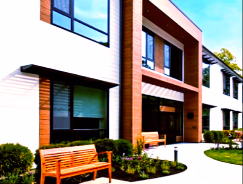 Modern senior living building exterior with benches, landscaping, and a glass entrance.