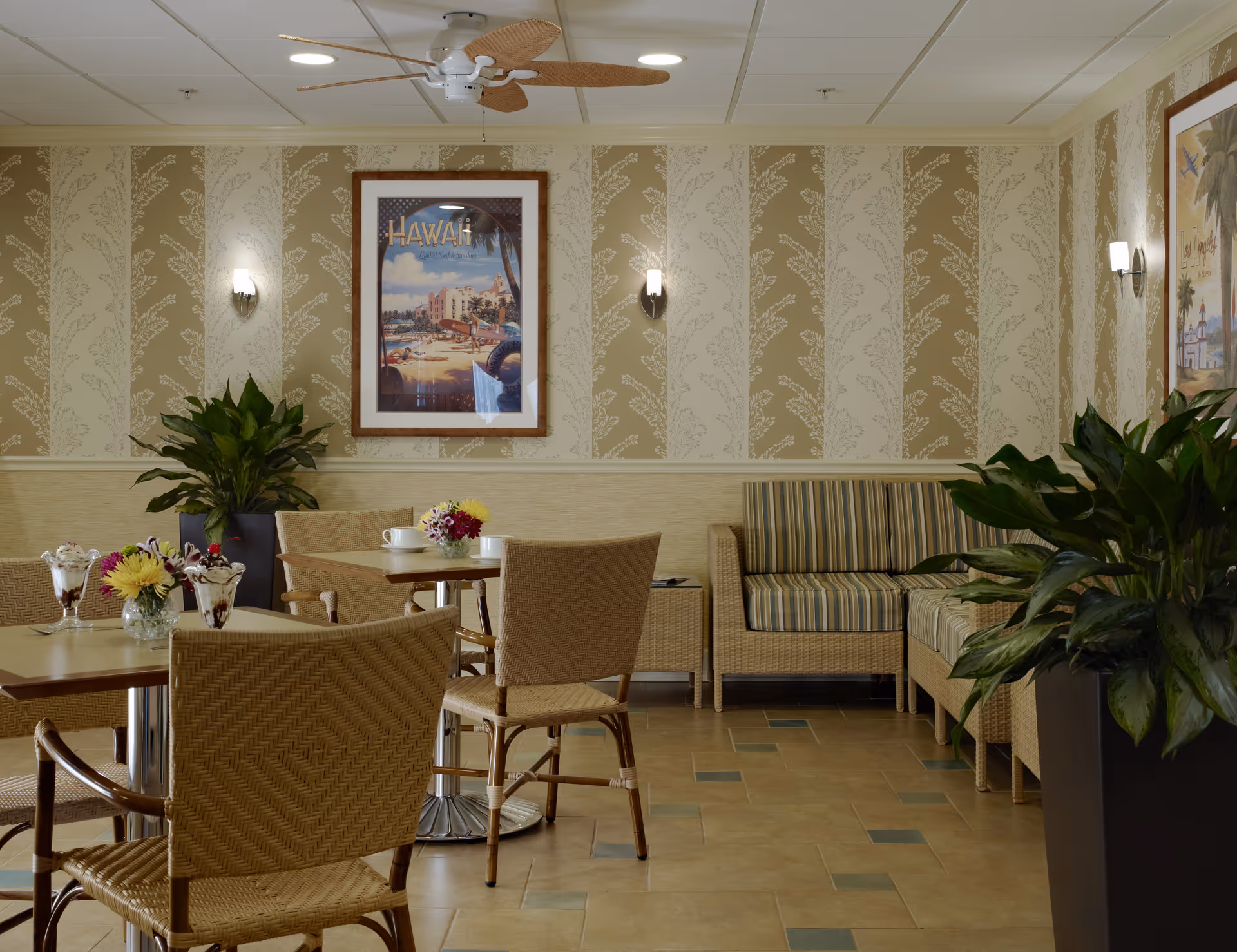 Interior lounge at Alden Estates of Naperville with wicker chairs, tables, plants, and wallpaper.
