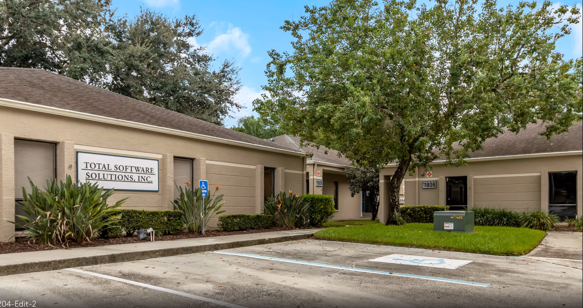 Exterior view of a single-story building with signage, greenery, and a parking area.