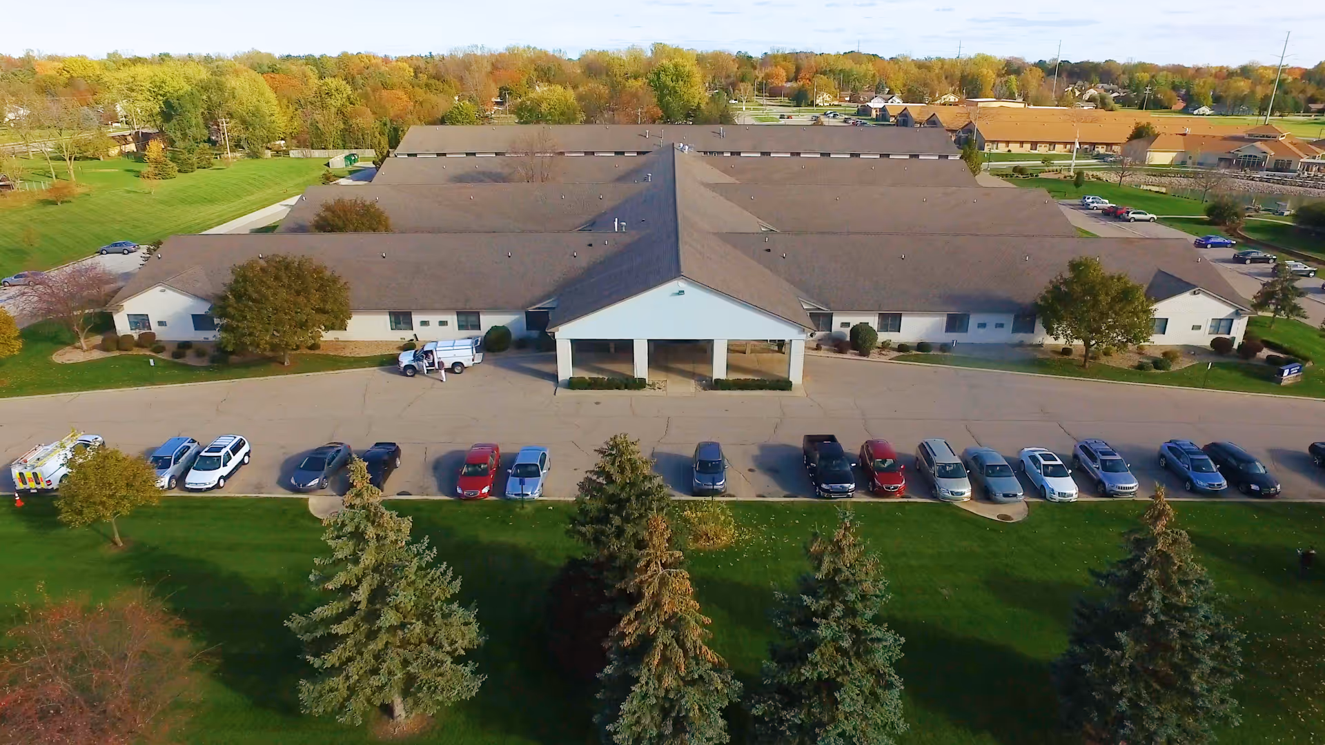 Aerial view of Wellspring Lutheran Services Senior Living Campus - Independent Living building with a large parking lot in front, surrounded by green lawns and trees with autumn foliage.