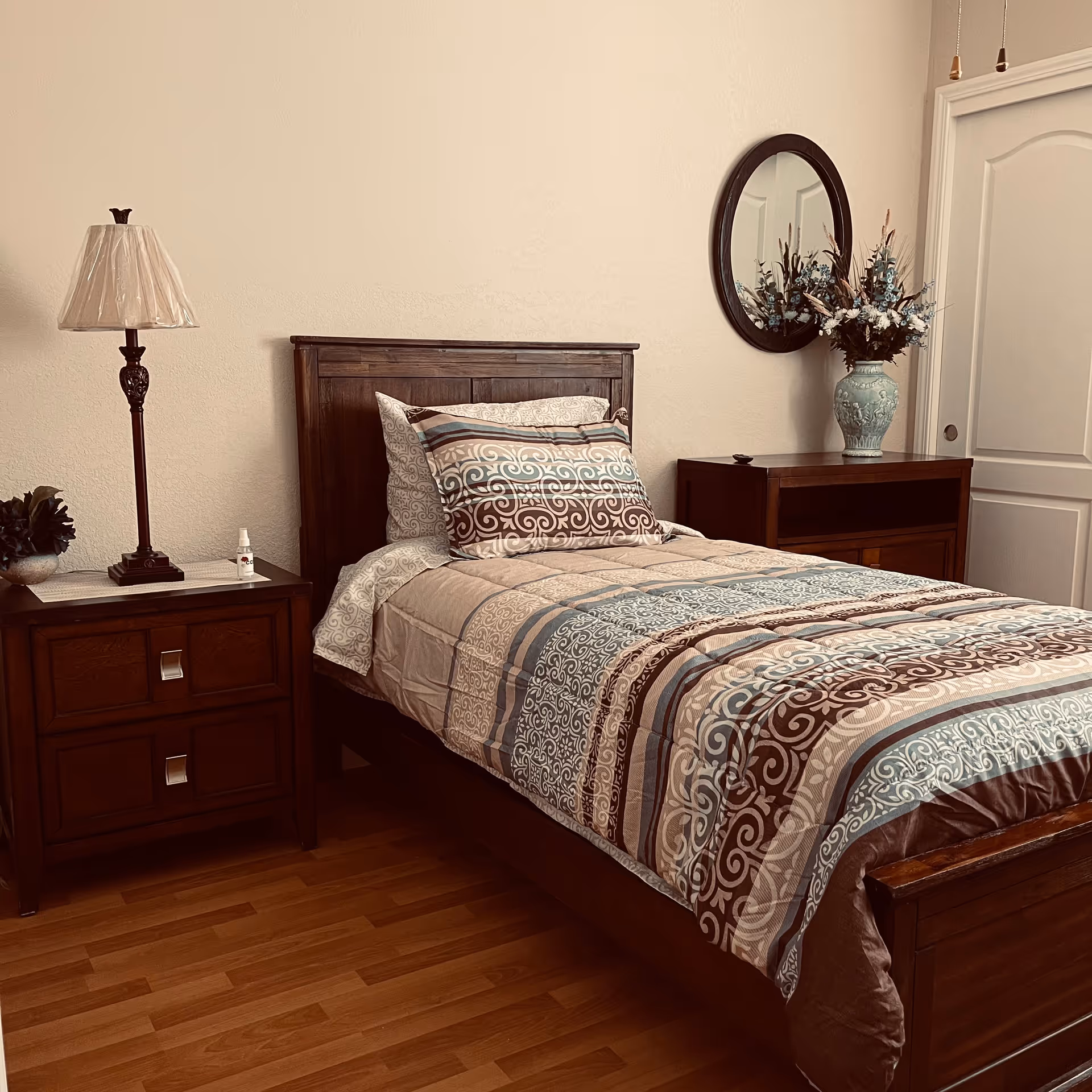 A neatly made wooden bedroom with nightstands, lamp, mirror, and floral decor.
