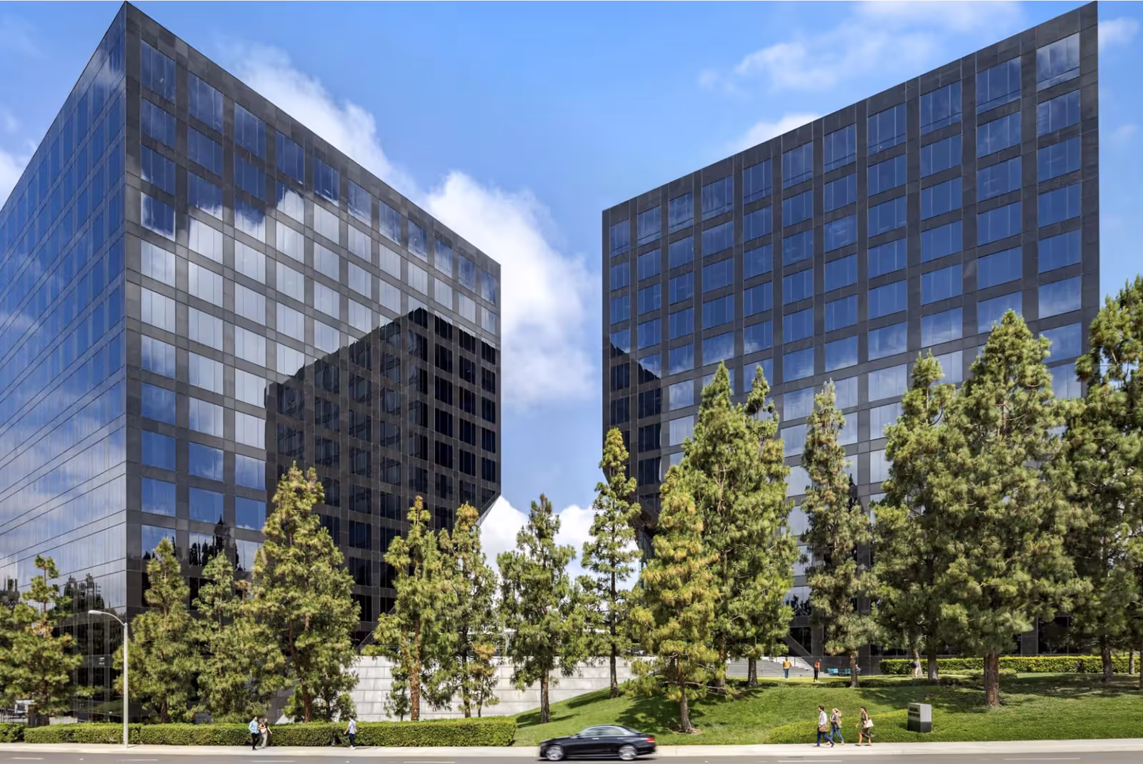Two modern glass buildings with reflecting windows and a row of trees in front.
