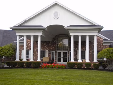 Front view of a brick senior living facility with white columns and manicured lawn.