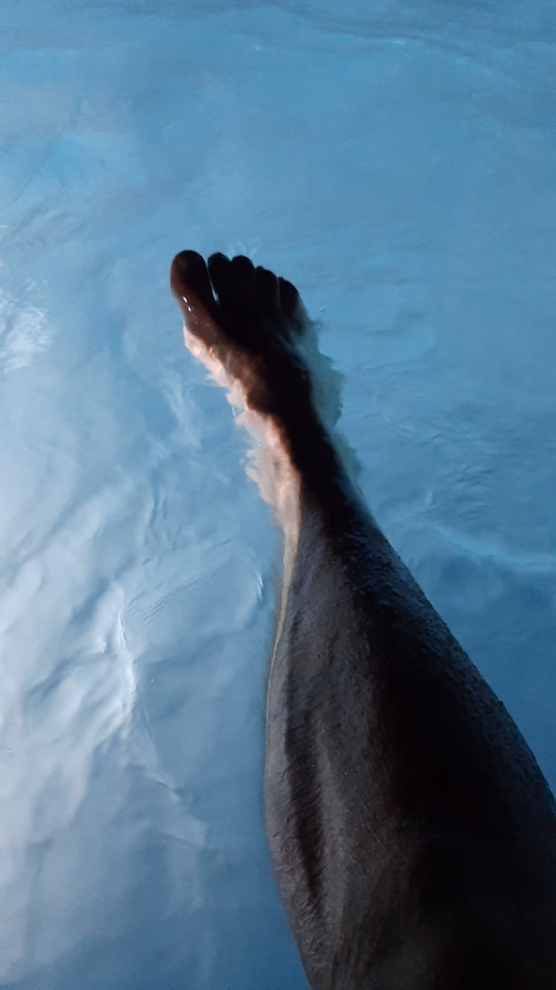 A leg and foot submerged in blue pool water, viewed from above.