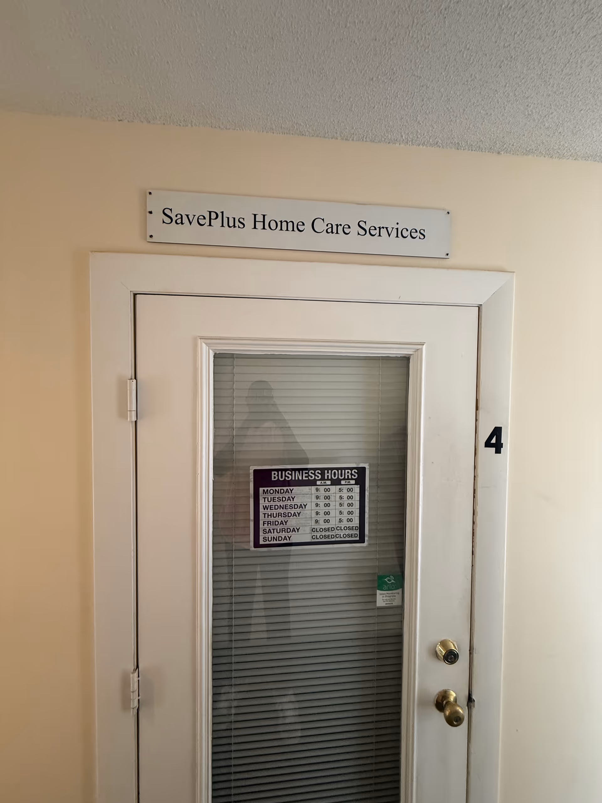 Interior hallway door labeled SavePlus Home Care Services with hours posted on window
