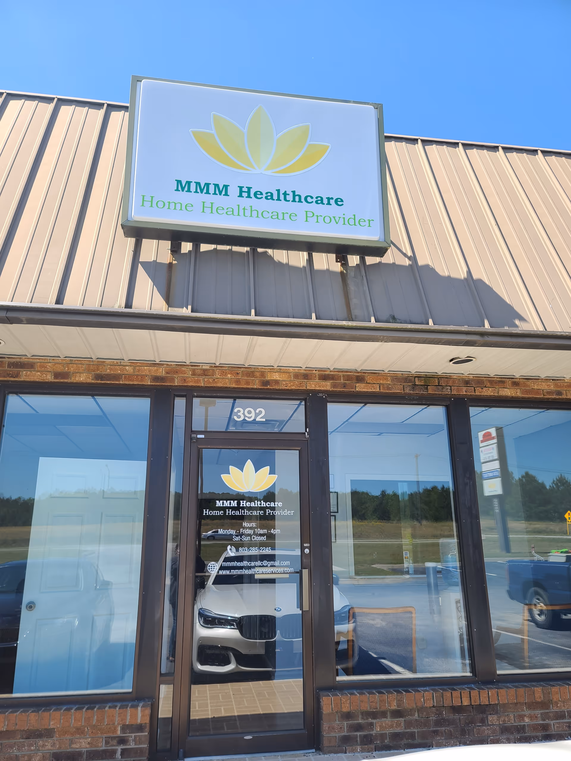 Exterior view of MMM Healthcare building with sign, entrance door, and parking reflected in glass.
