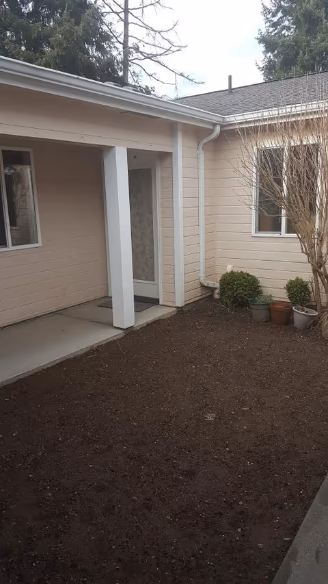 Front entrance of a beige building with a small covered porch and dirt yard.
