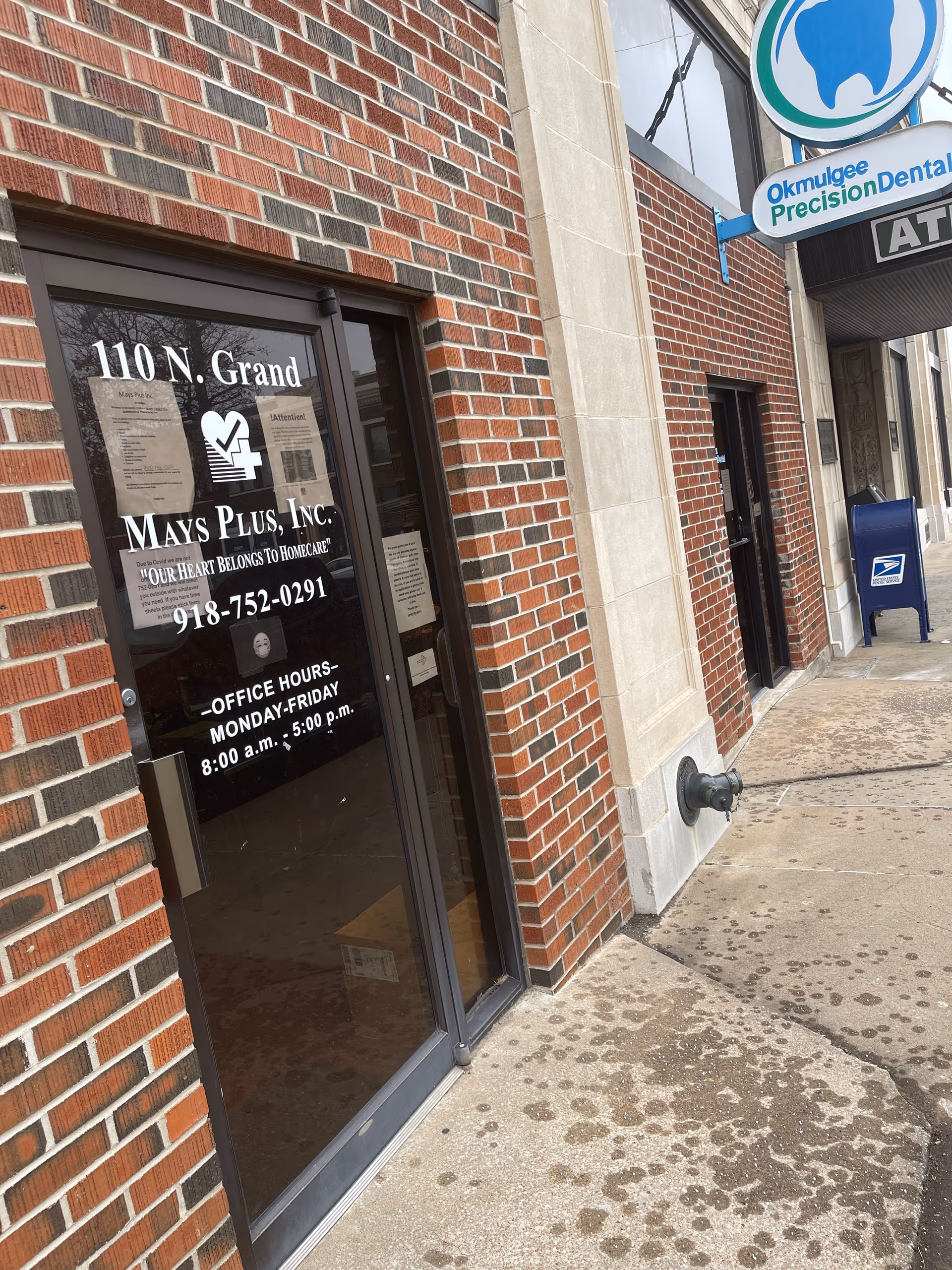 Brick building entrance with Mays Plus signage and glass door.