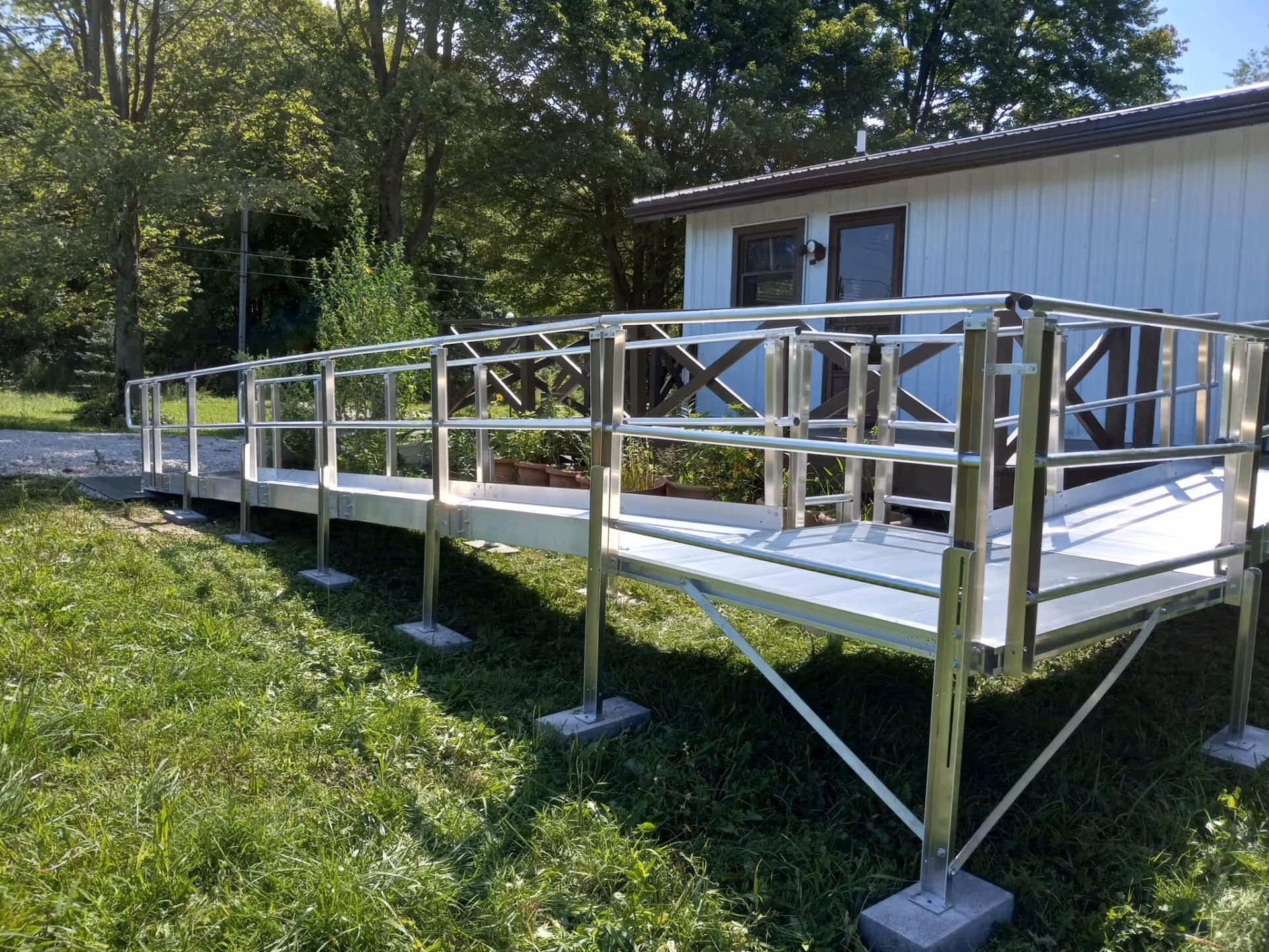 Silver metal wheelchair ramp extends from a small building outdoors, surrounded by trees and grass.