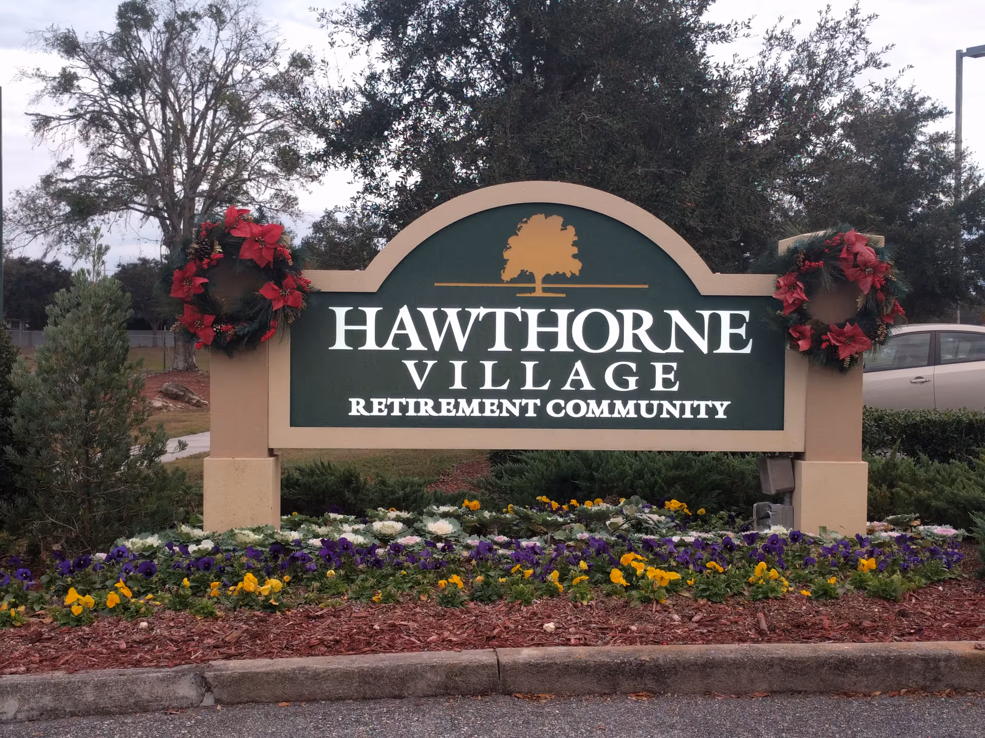 Outdoor Hawthorne Village retirement community sign with red wreaths and flowers.