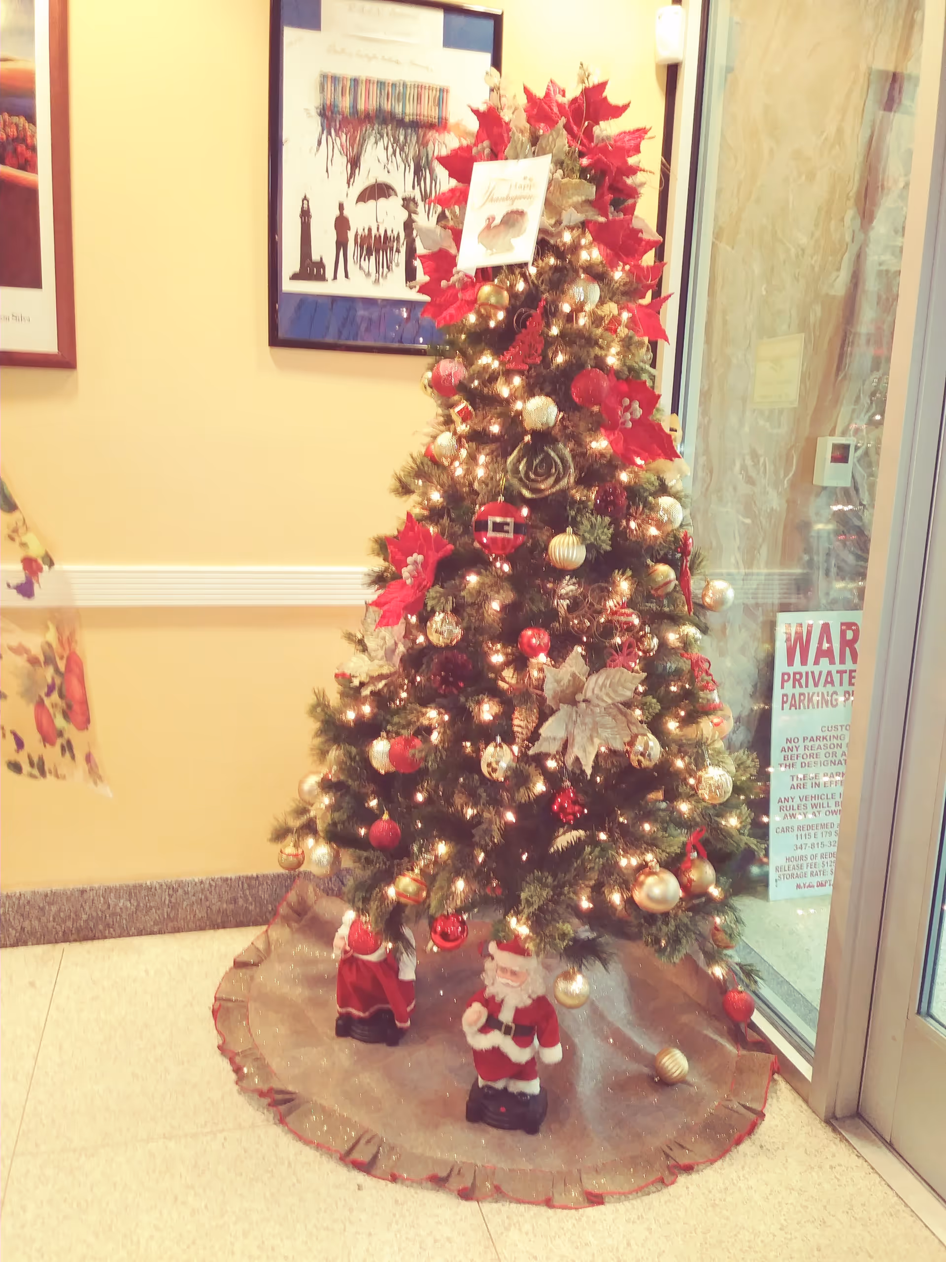 Decorated Christmas tree beside glass doors in a warmly lit senior living lobby.