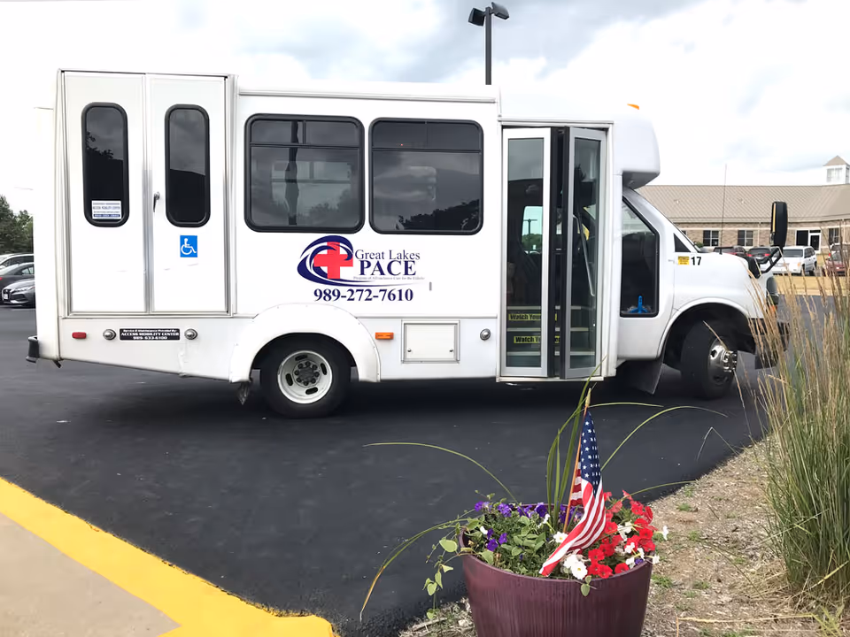 White Great Lakes PACE shuttle bus parked in lot with open door and flower pot.