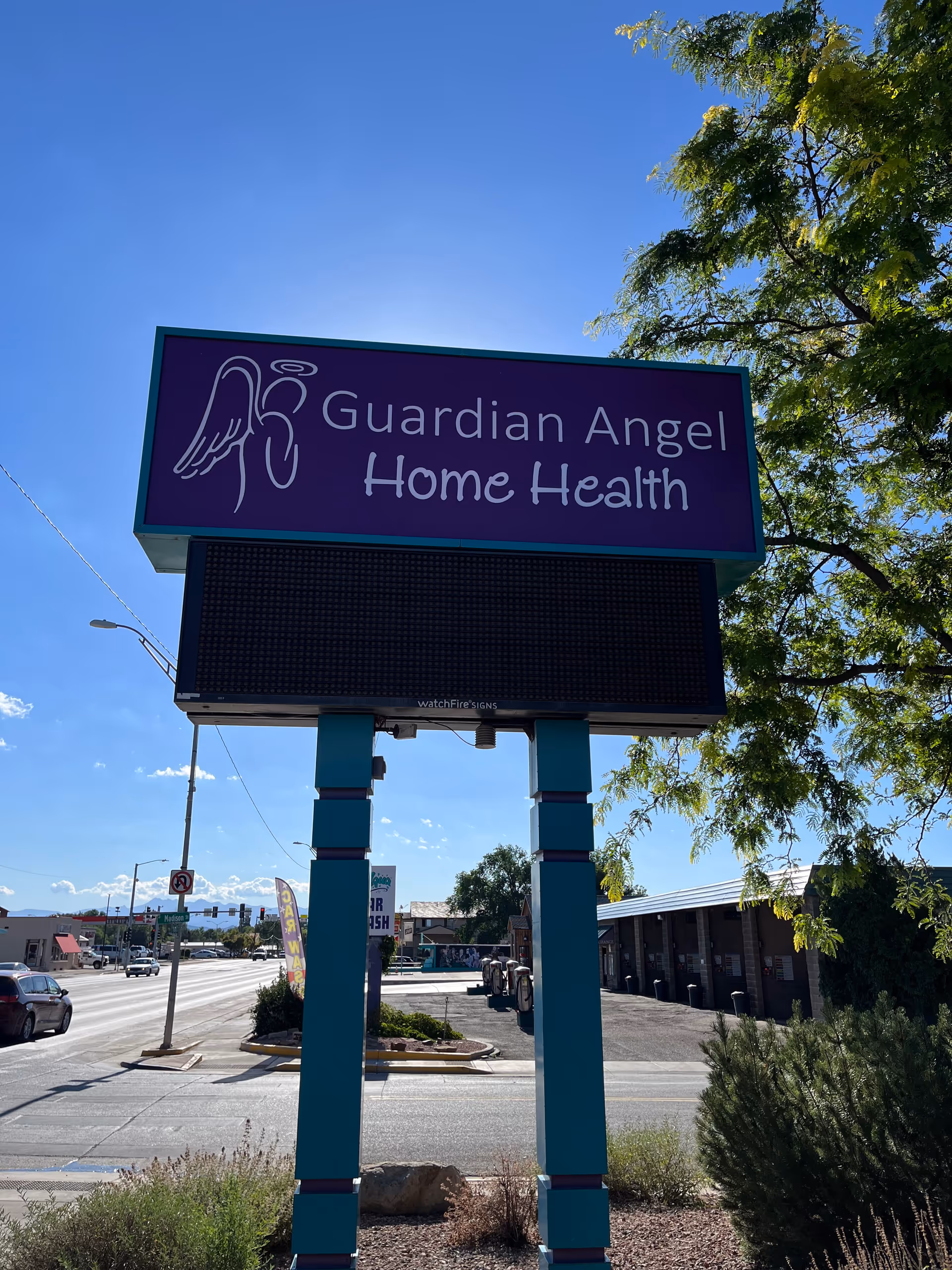 Blue sign reading Guardian Angel Home Health stands outside a building in a parking lot.