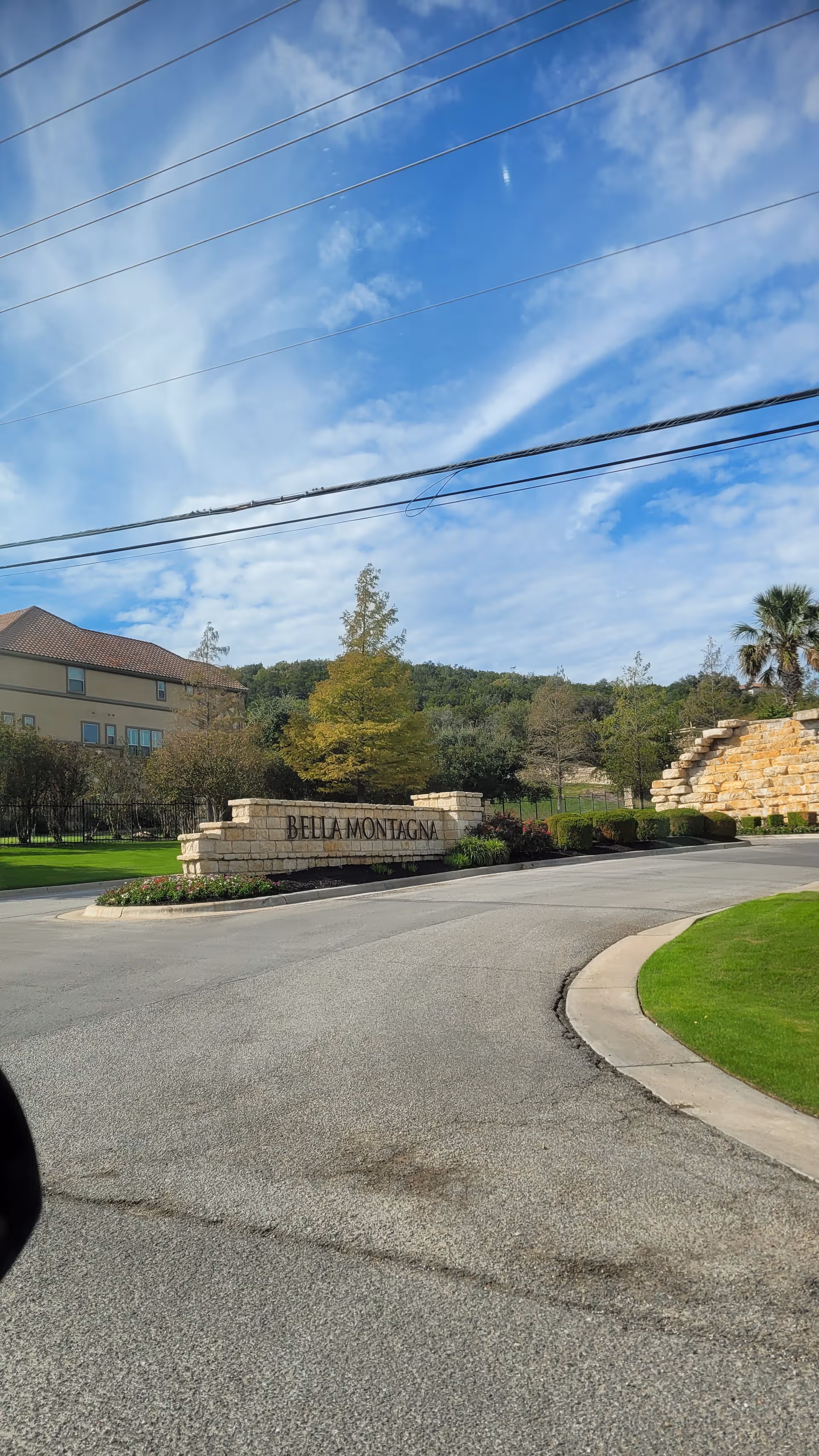 Outdoor entrance with stone sign and manicured landscaping against a blue sky.