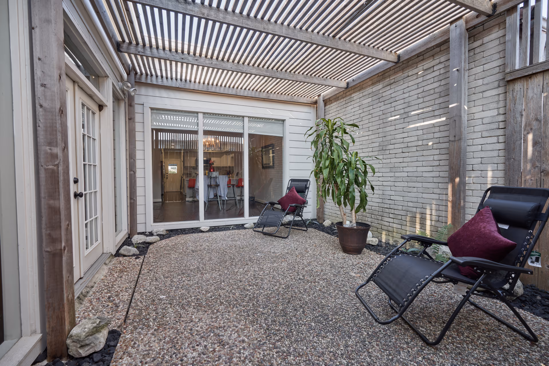 Outdoor patio with gravel floor, lounge chairs, potted plant, and sliding glass door.