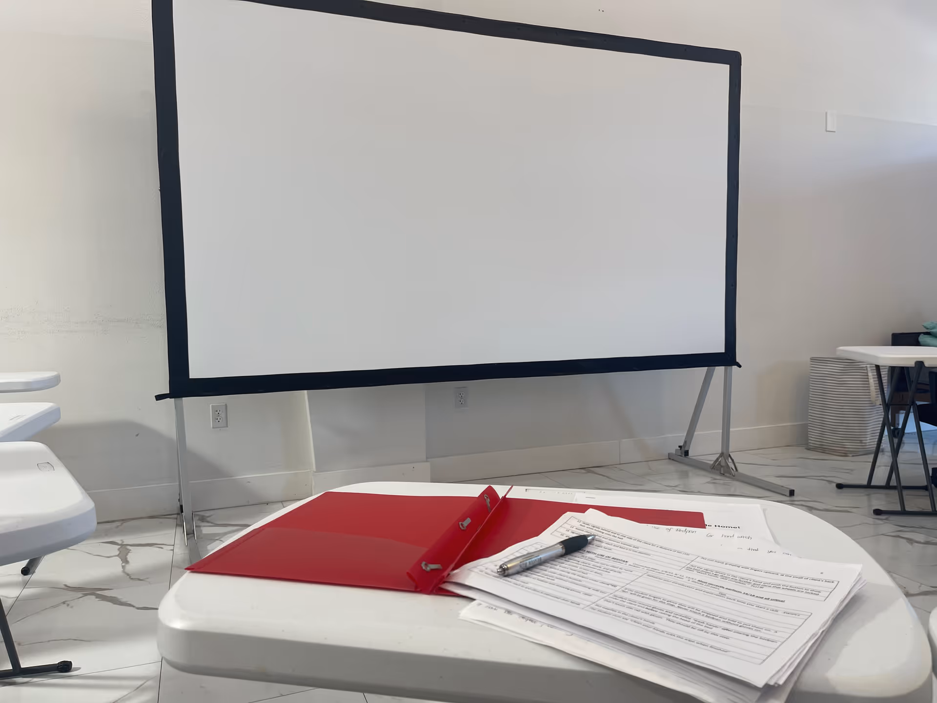 A large portable projection screen set up in a bright interior room with tables and papers.