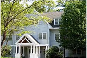 Two-story gray building with a white front porch, surrounded by trees.