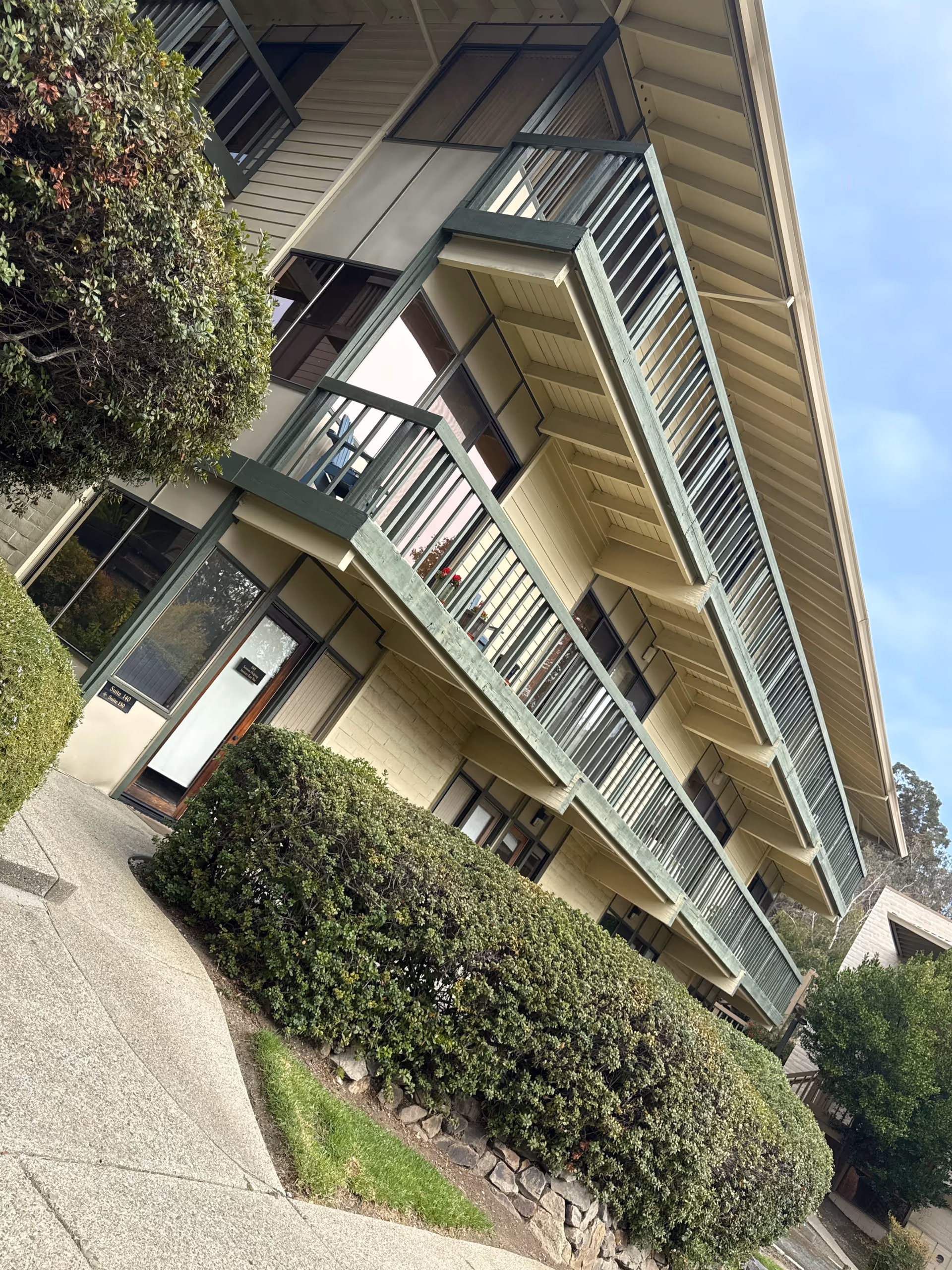 Multi-story beige senior living building with balconies and manicured shrubs along walkway.
