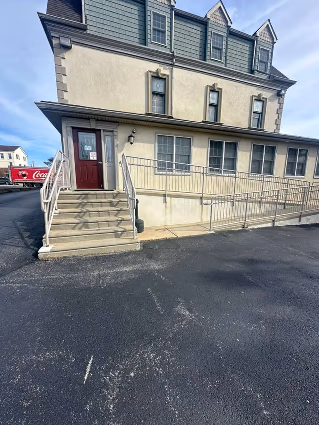 Two-story beige building with a red door and accessible ramp at the entrance.
