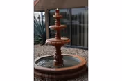 A three-tier fountain in a gravel courtyard beside a glass-walled building.