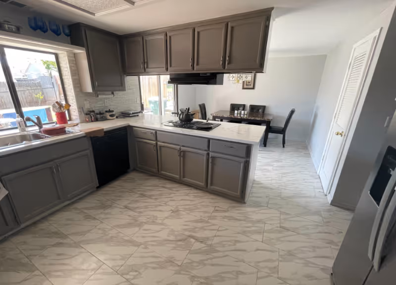 Modern kitchen with gray cabinets, marble-like countertops, island, and adjacent dining area.