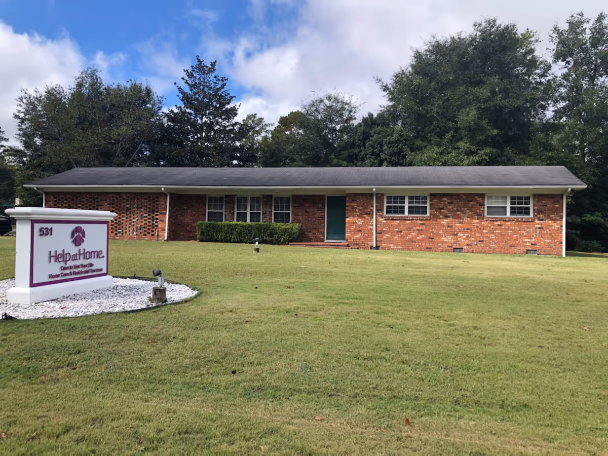 Front view of a single-story brick senior facility with a Help at Home sign.